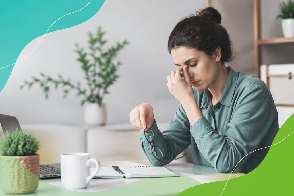 A tired young woman sitting in a cozy home office, rubbing her eyes in frustration, surrounded by plants and soft natural light, symbolizing chronic fatigue.